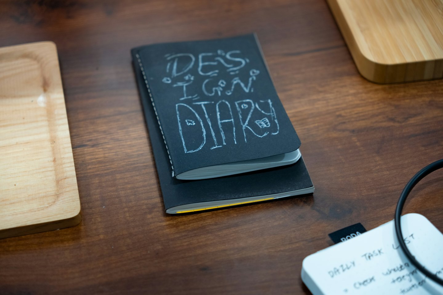 Two notebooks and wooden trays on a dark desk surface.