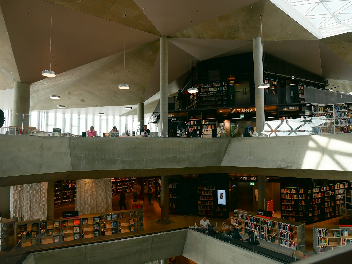 People work on laptops inside a multi-level concrete library.