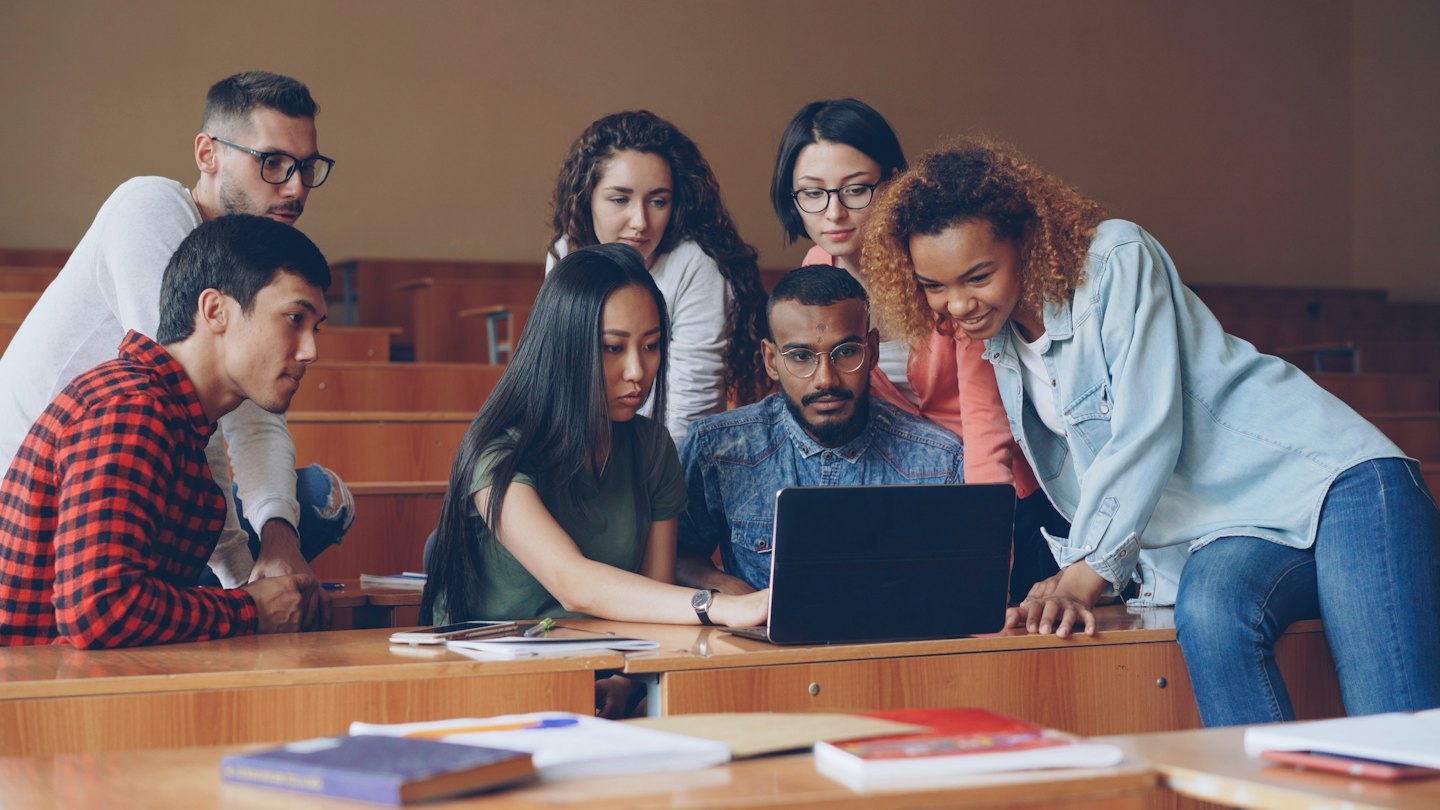 University students collaborating around a laptop in a lecture hall.
