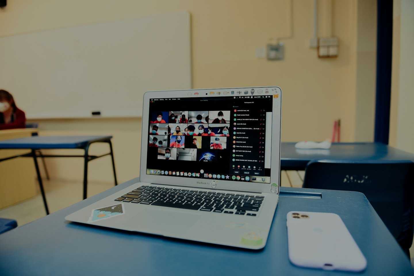 Laptop shows video conference on a blue classroom desk.