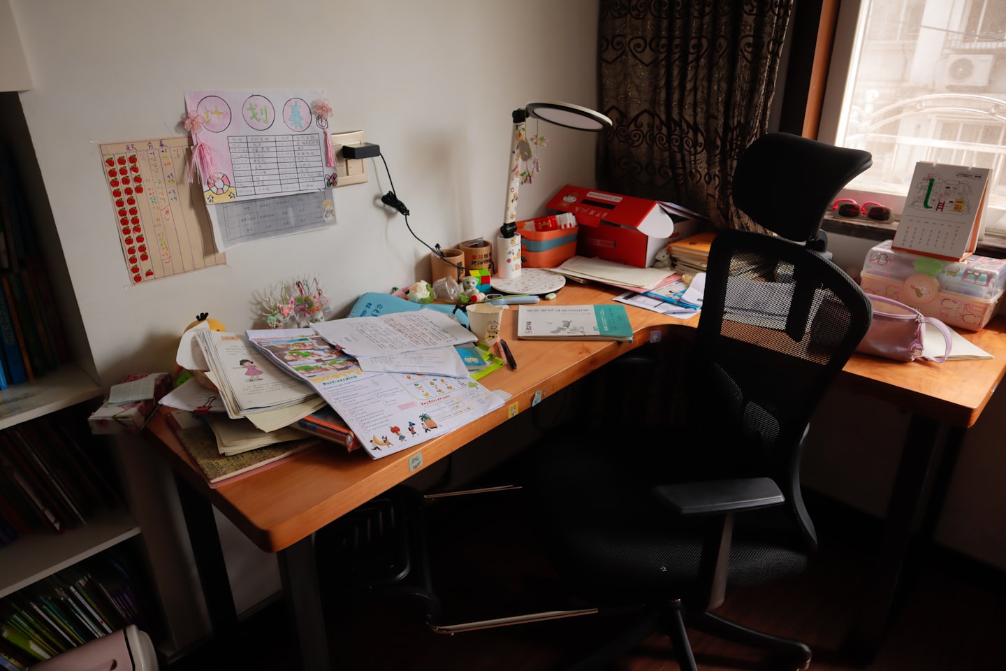 Cluttered wooden study desk with books and hand-drawn wall charts.