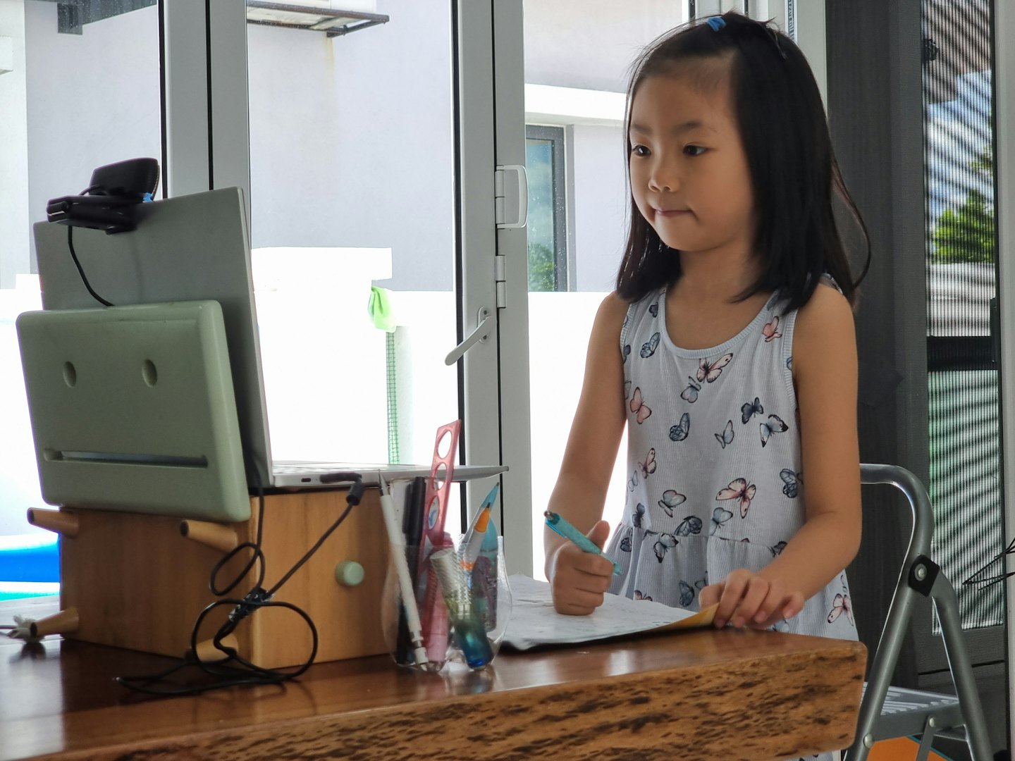 Young girl writing at a desk with a laptop.